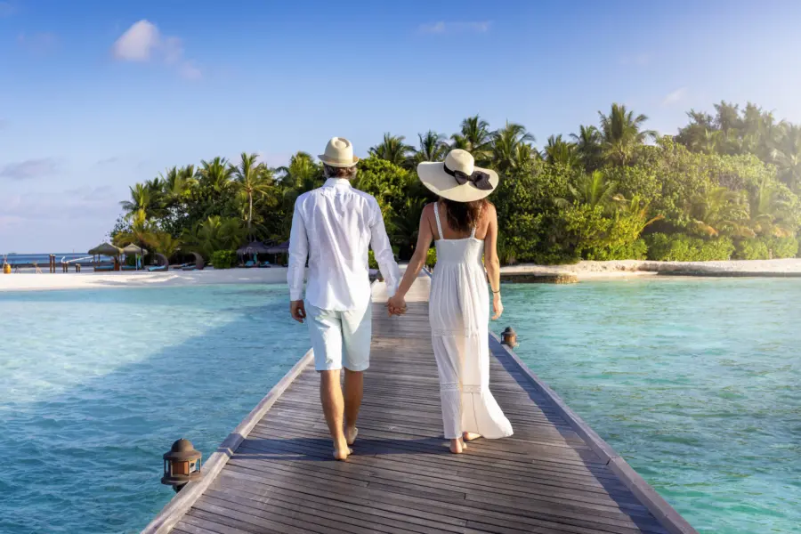 Avila Reizen Malediven romantic couple A elegant couple walks down a wooden pier over turquoise sea in the Maldives islands